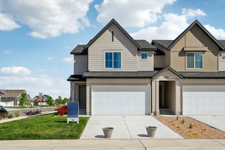 Two-story residence featuring light-toned siding, attached two-car garage, pitched rooflines, and a low-maintenance landscape