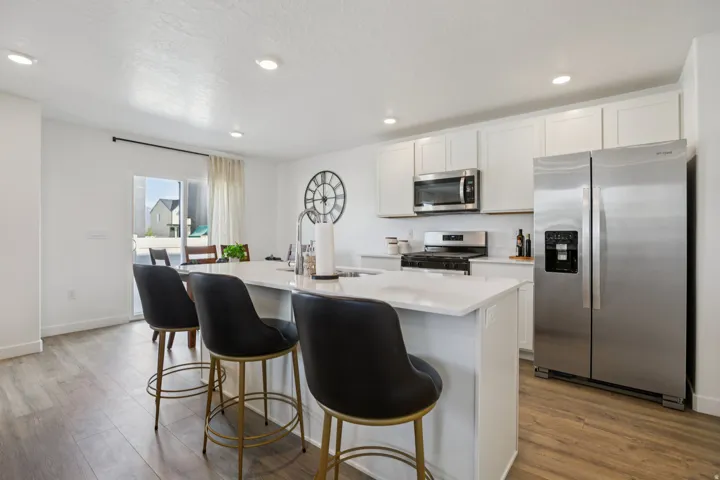 Kitchen featuring white cabinetry, stainless steel appliances, a center island with countertop seating, and wood-finish flooring