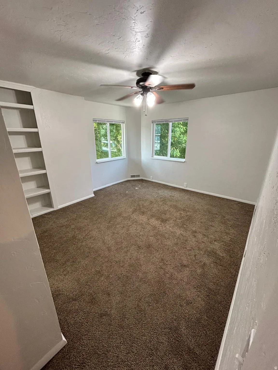 Built-in shelving, two windows, ceiling fan with integrated lighting, and carpeted flooring