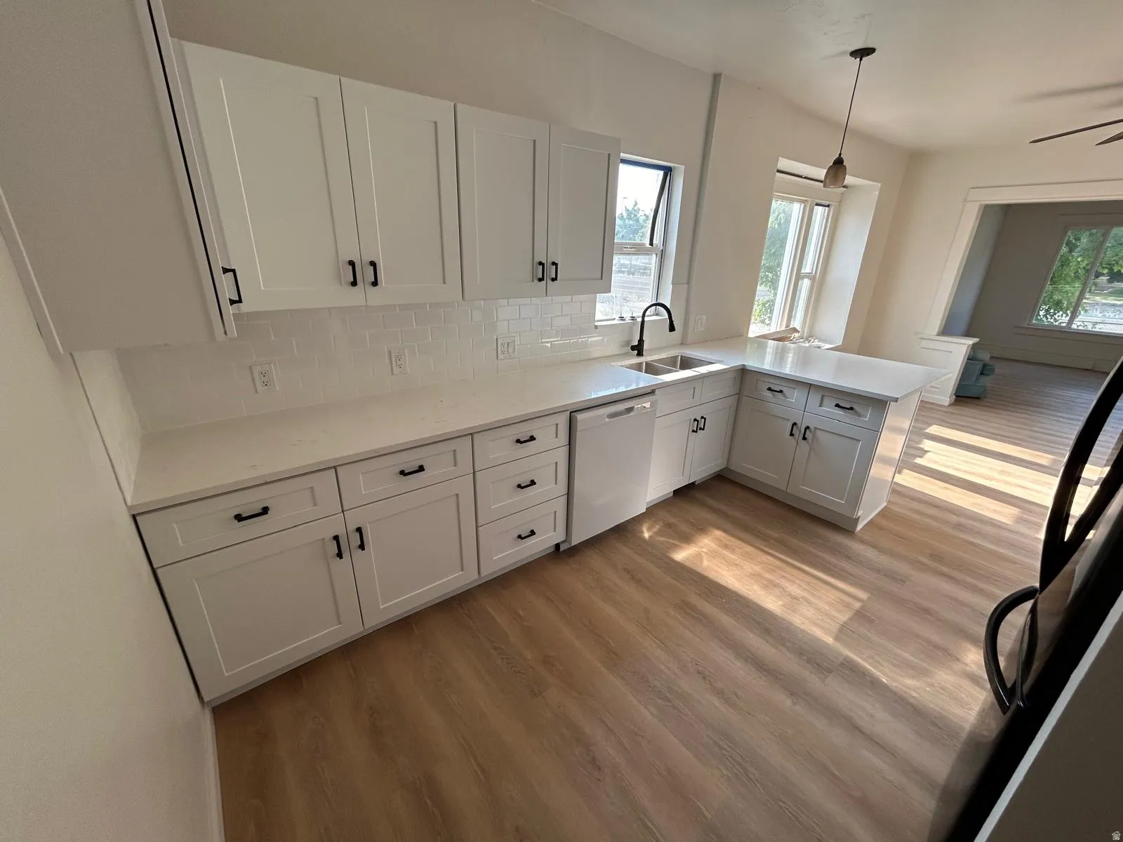 White cabinetry, white countertops, subway tile backsplash, stainless steel sink, and wood-finish flooring