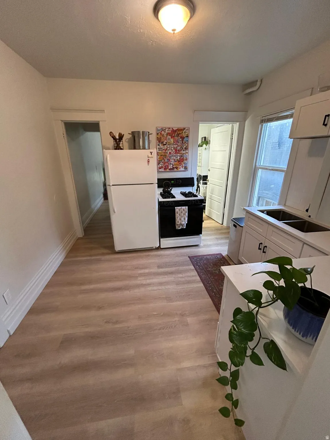 Kitchen featuring wood-finish flooring, white cabinetry, a double basin sink, and a four-burner stove