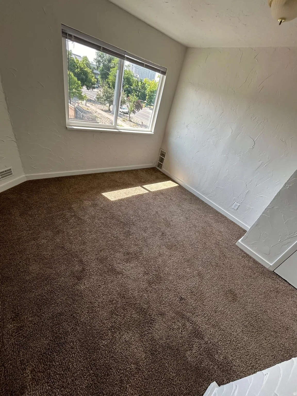 Sloped ceiling room featuring a large window with blinds and plush carpeting