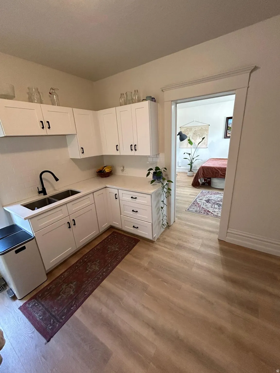 White flat-panel cabinetry, light wood-finish flooring, white countertops, dual basin stainless steel sink with a matte black faucet, and white subway tile backsplash