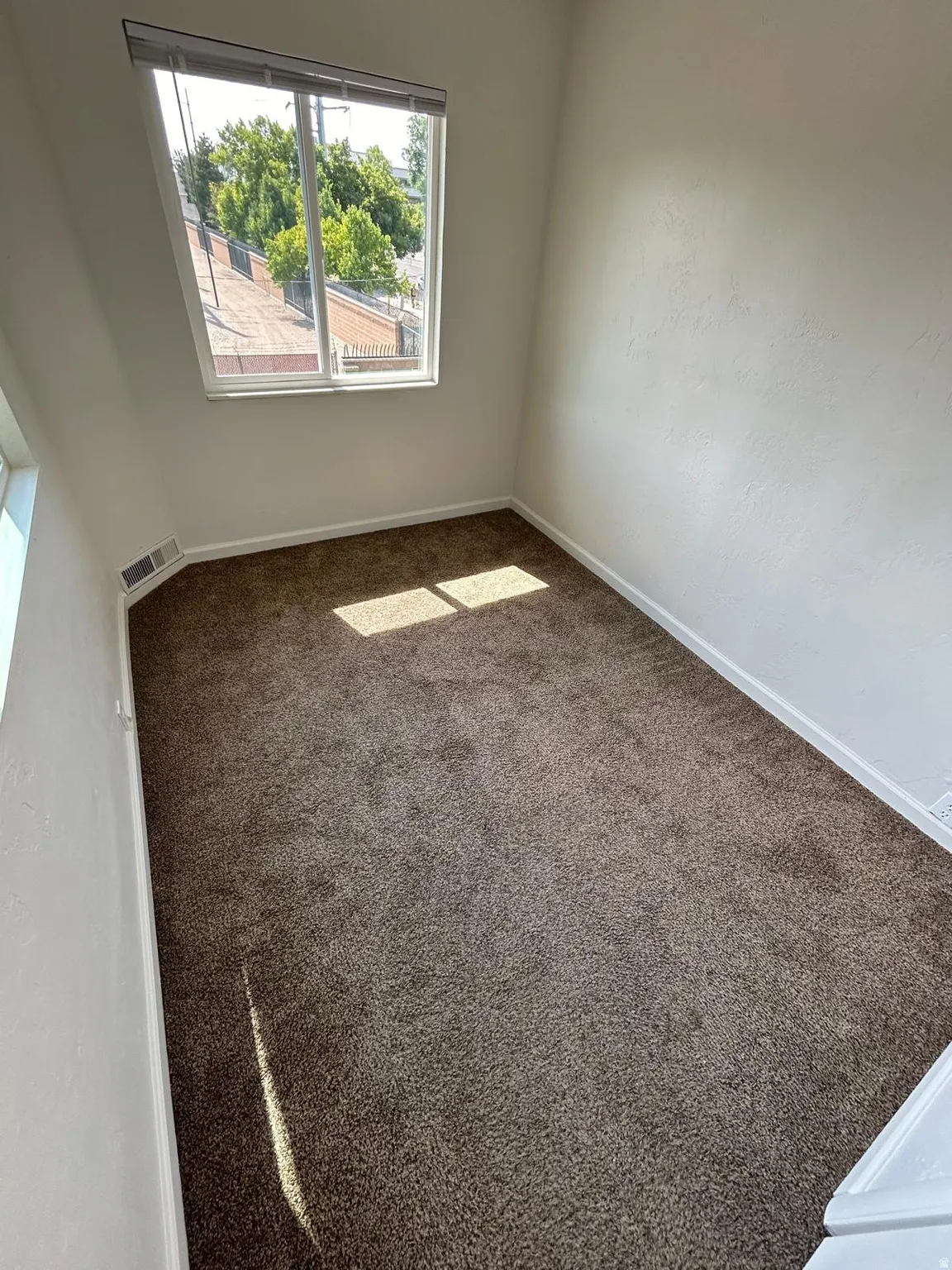 Carpeted room with a large window and white walls
