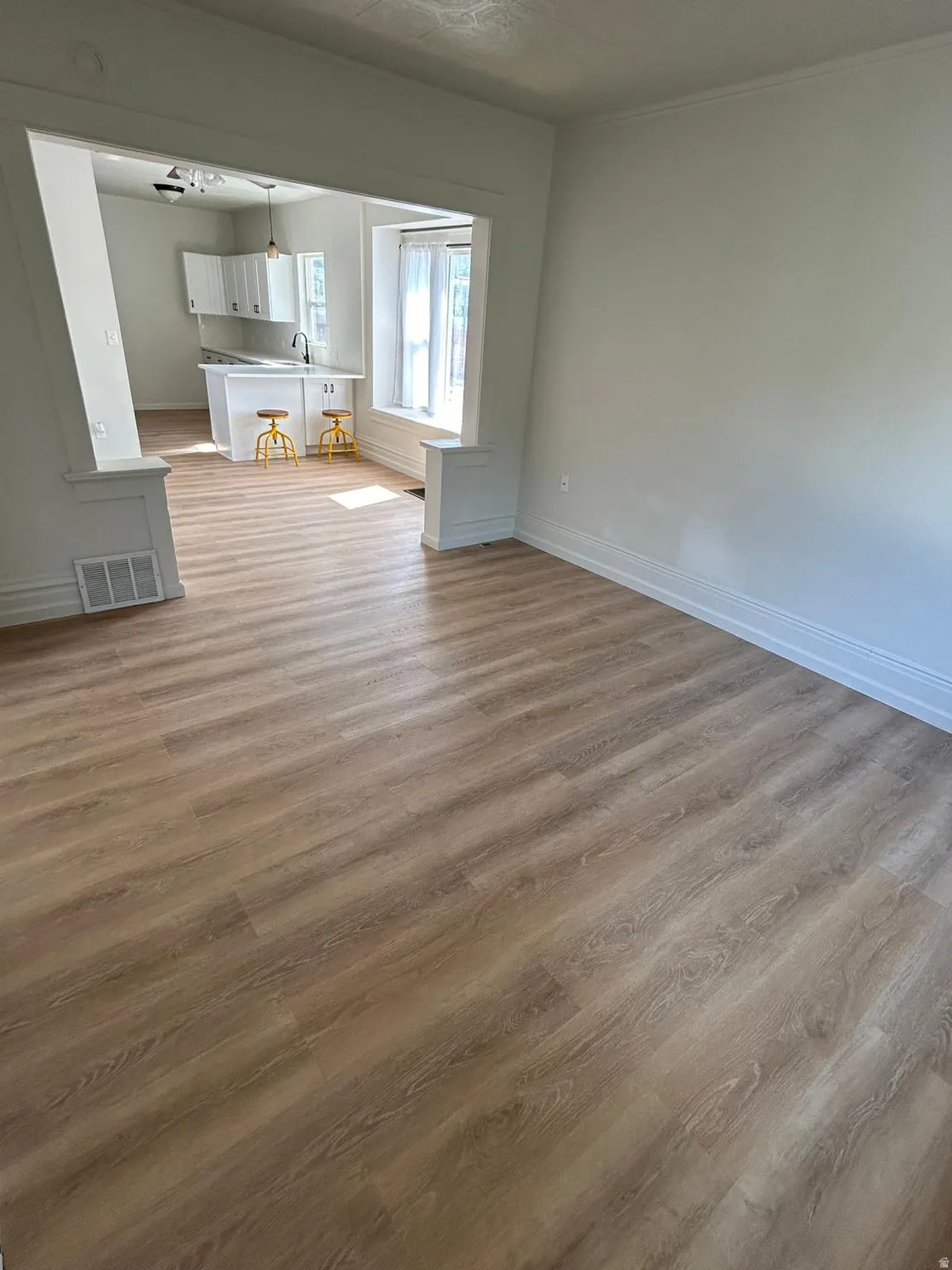 Wood-finish flooring throughout, white walls, and an open archway to the kitchen