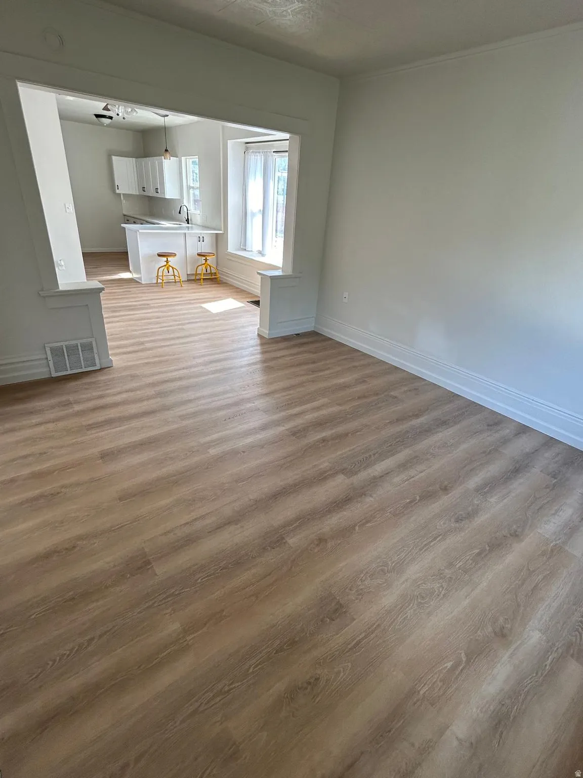 Wood-finish flooring throughout, bright white walls, and a kitchen featuring white cabinetry, a central island, and a dark faucet