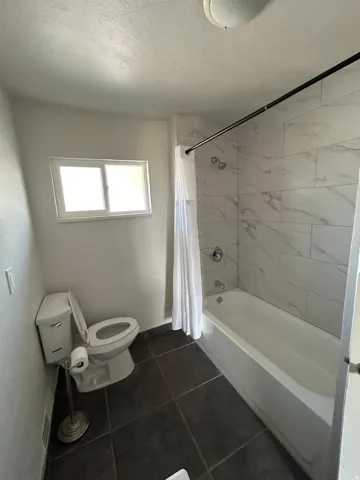 Bathroom featuring a full bathtub with tile surround, a single window, and dark tile flooring