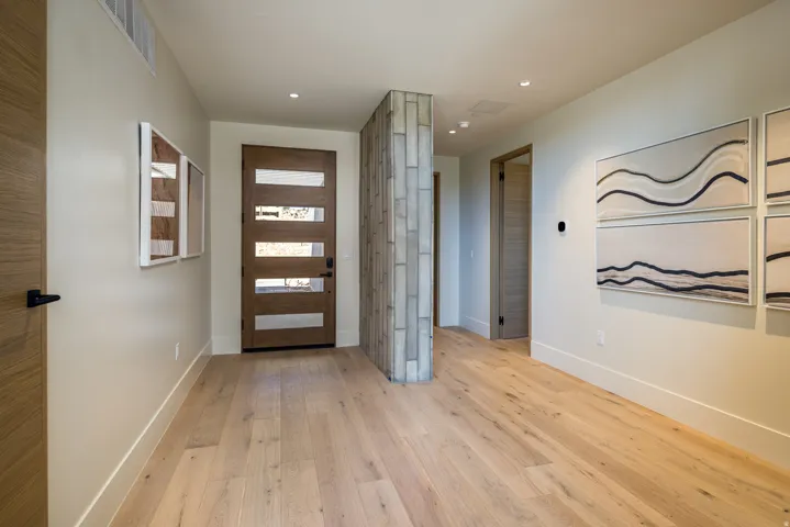 Entryway featuring a modern wood-finish door with frosted glass panels, wide plank wood-finish flooring, a textured stone-finish accent wall, recessed lighting, and crisp white baseboards