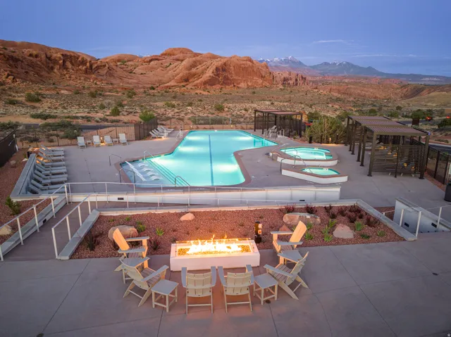 Outdoor amenity area featuring a large illuminated swimming pool, two integrated spas, and a fire pit with surrounding seating