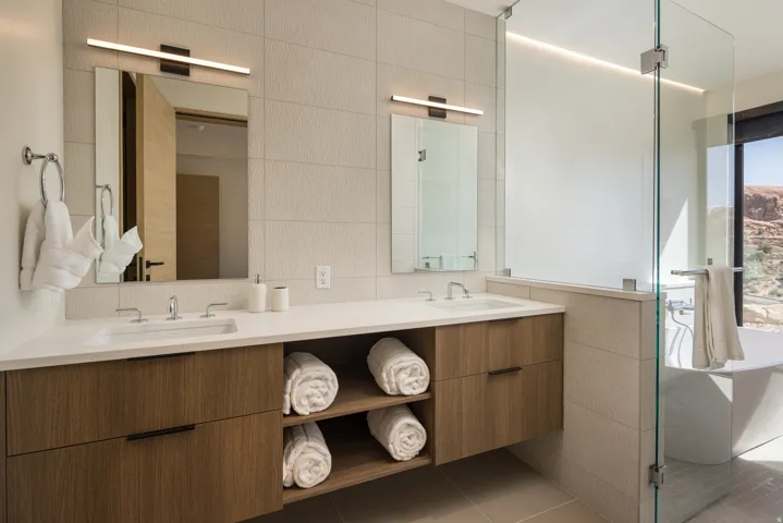 Dual vanity featuring wood-finish cabinetry, integrated open shelving, and white countertops