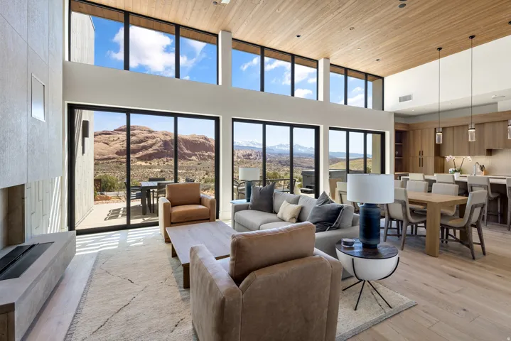 Expansive living space featuring a wood-panel ceiling, full-height windows, a linear fireplace, wood-finish flooring, and a stone accent wall