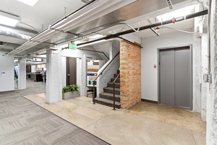 Exposed brickwork accenting a carpeted staircase, polished concrete flooring, and a contemporary elevator