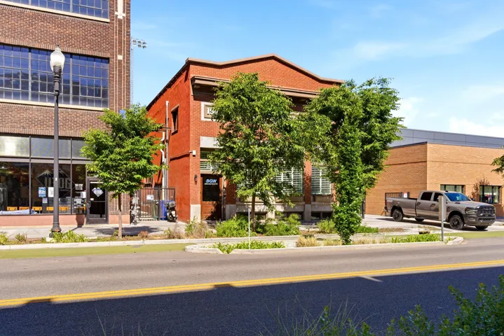 Red brick exterior with multiple windows, featuring mature trees and street-level access