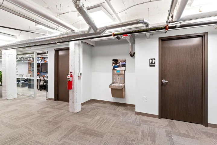 Commercial space featuring exposed overhead ductwork, patterned carpet tile flooring, and dark wood-finish doors