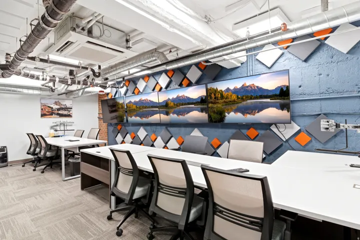 Open-concept office space featuring exposed ductwork, textured accent wall with geometric panels, and integrated display screens