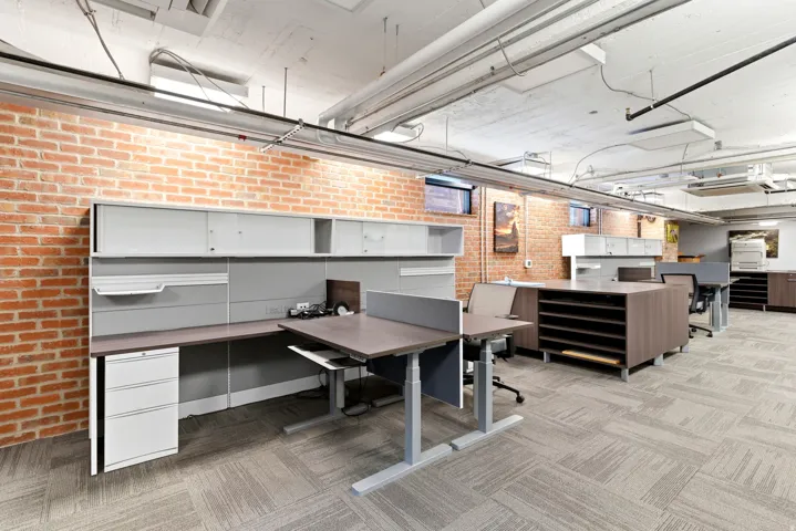 Exposed brick wall, carpet tile flooring, exposed ceiling utilities, built-in desk with storage, recessed windows