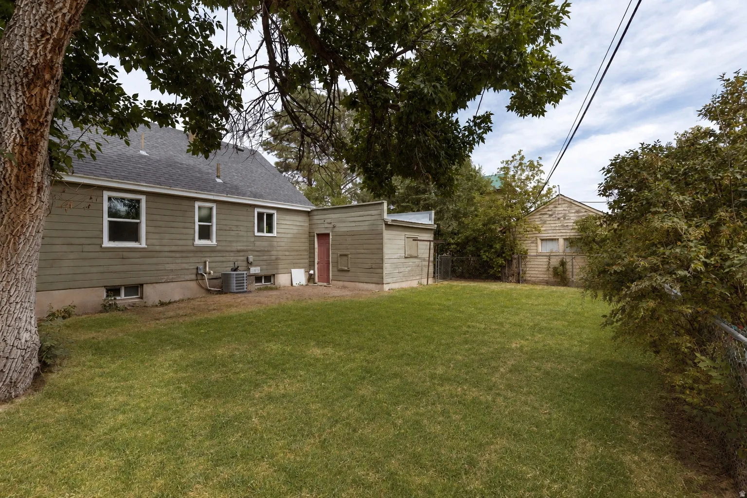 Expansive lawn area, mature trees, single-story detached structure, additional utility building, and a fenced perimeter