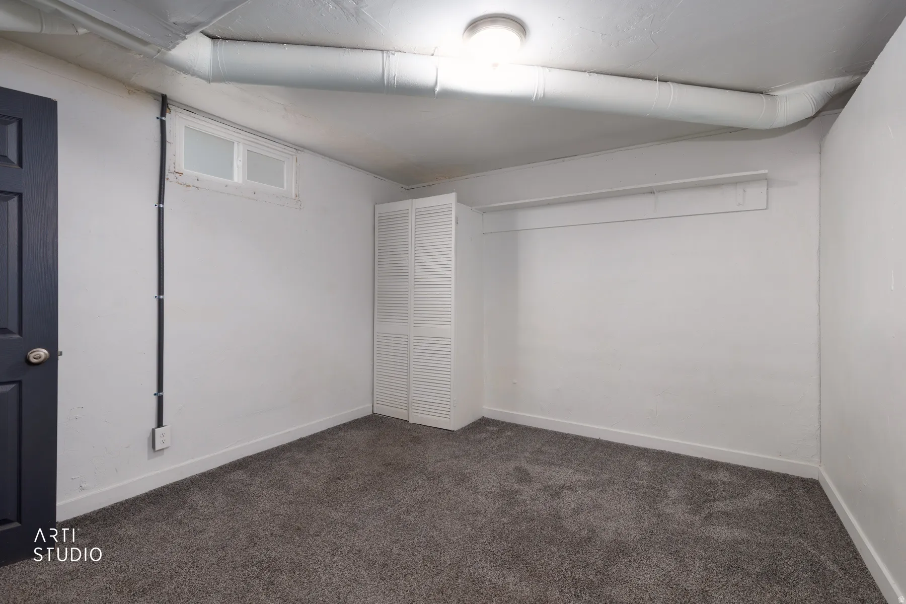 Carpeted interior space with white walls, a dark paneled door, and a louvered bi-fold door