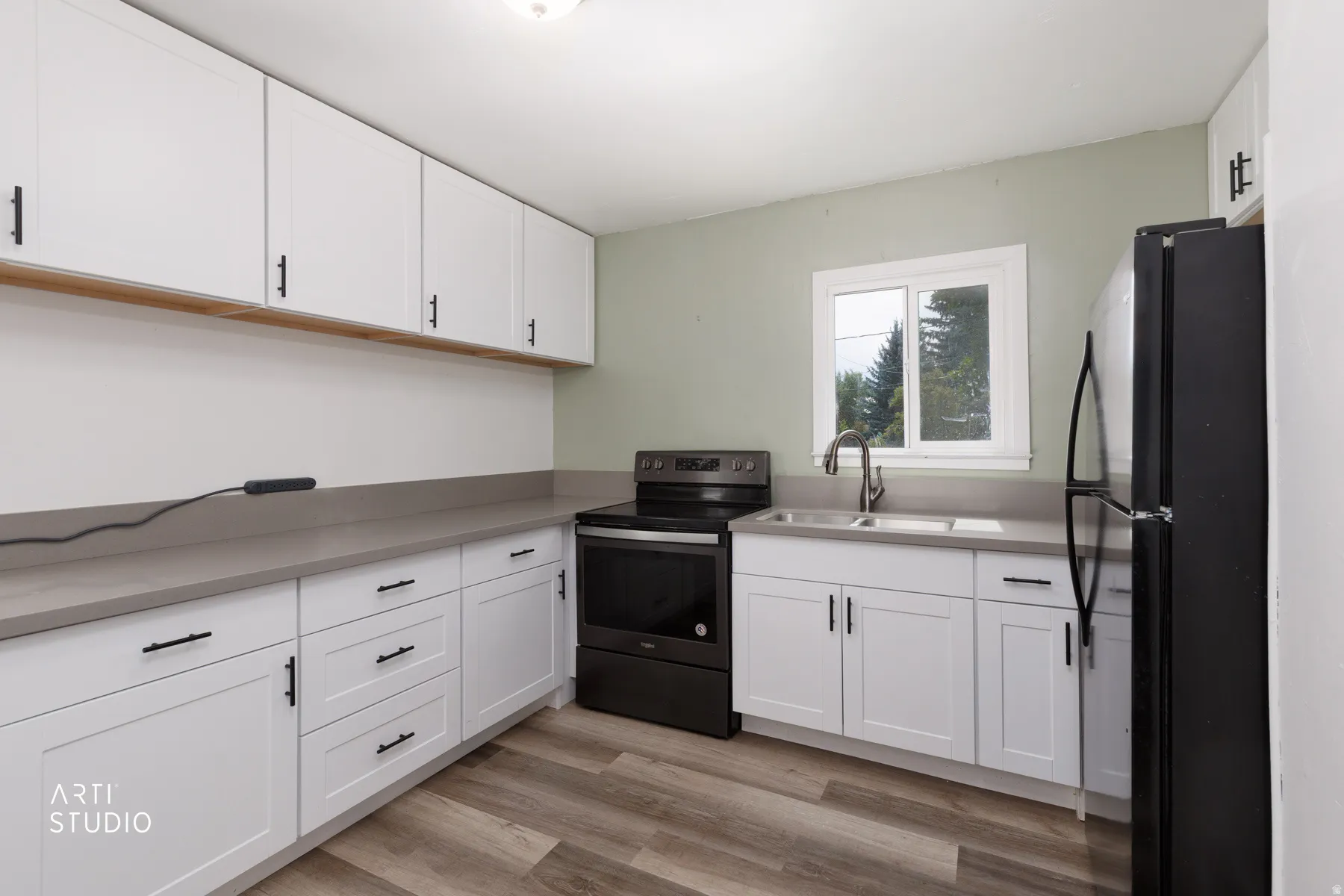 Modern kitchen featuring white shaker-style cabinetry with hardware accents, gray quartz countertops, black stainless steel appliances including a slide-in range and refrigerator, stainless steel sink with contemporary faucet, wood-finish flooring, and na