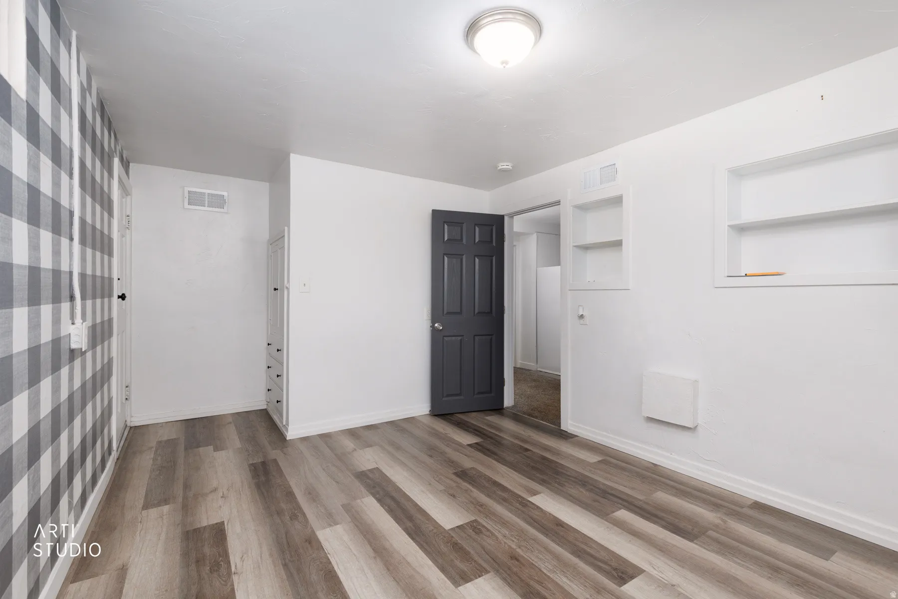 Wood-finish flooring, accent wall with plaid pattern, built-in shelving, built-in cabinetry, and a dark-toned door