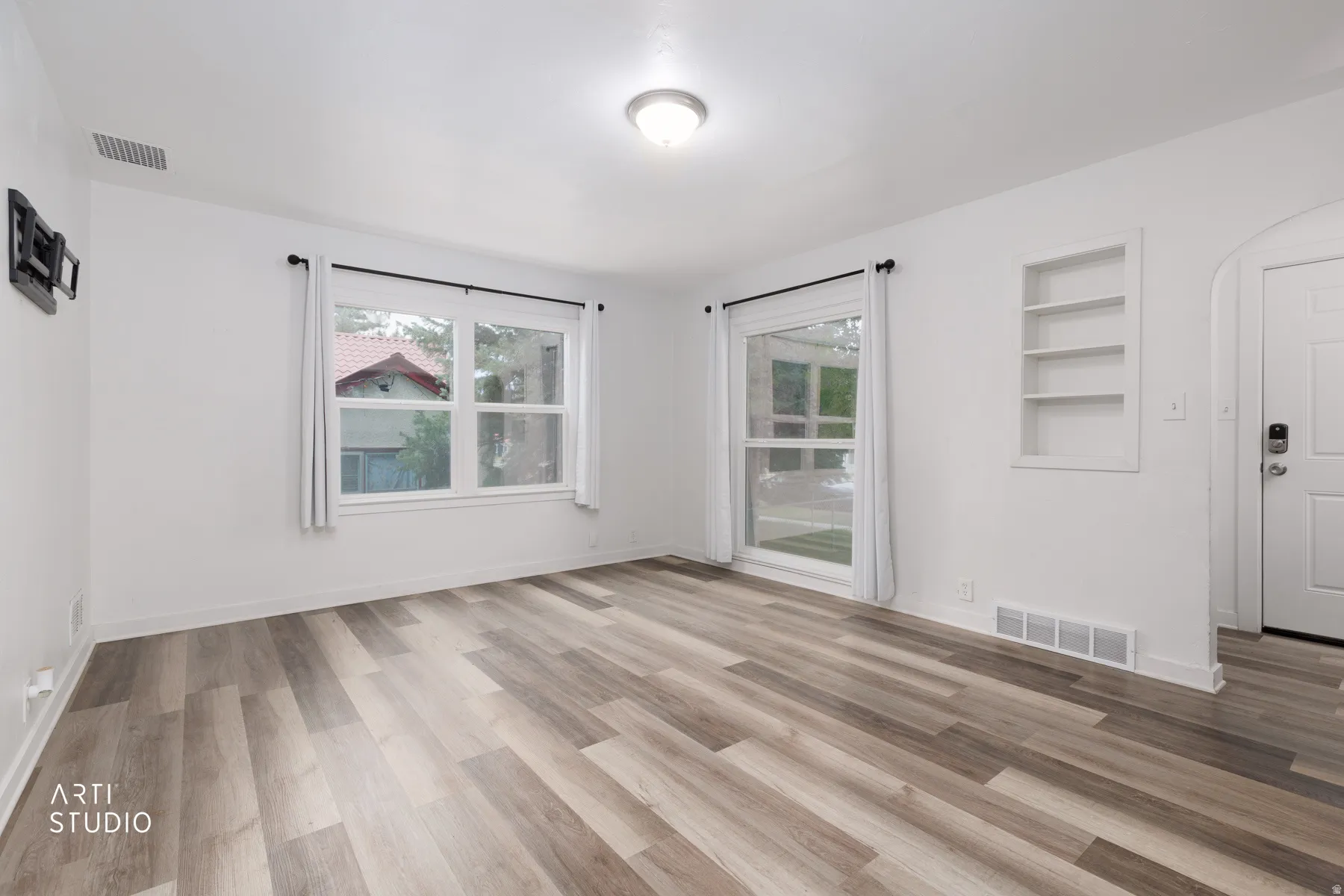Wood-finish flooring throughout, bright white walls, recessed wall shelving, and a prominent entry door