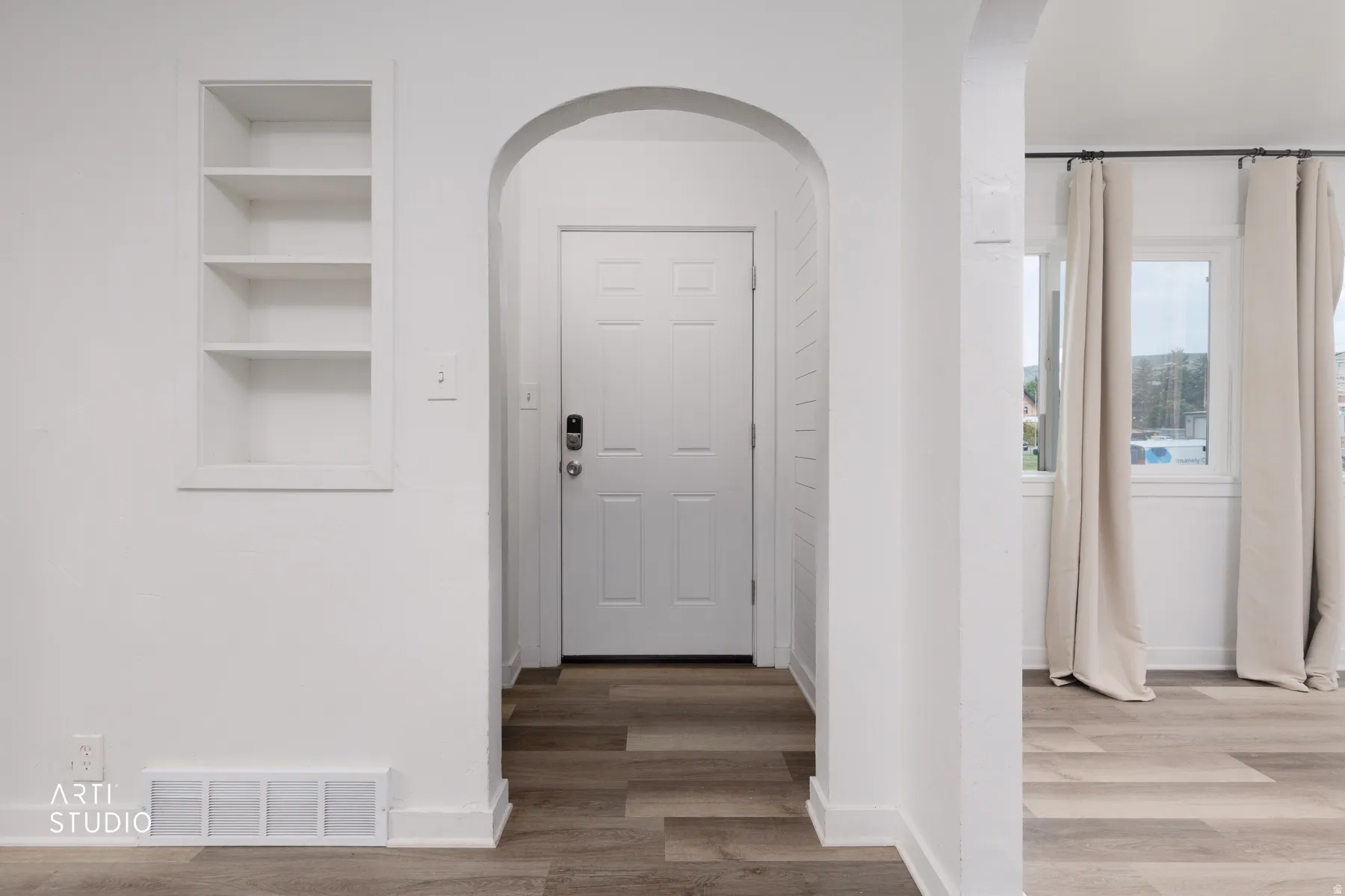Archway entry, built-in shelving, wood-finish flooring, white paneled door, multiple windows