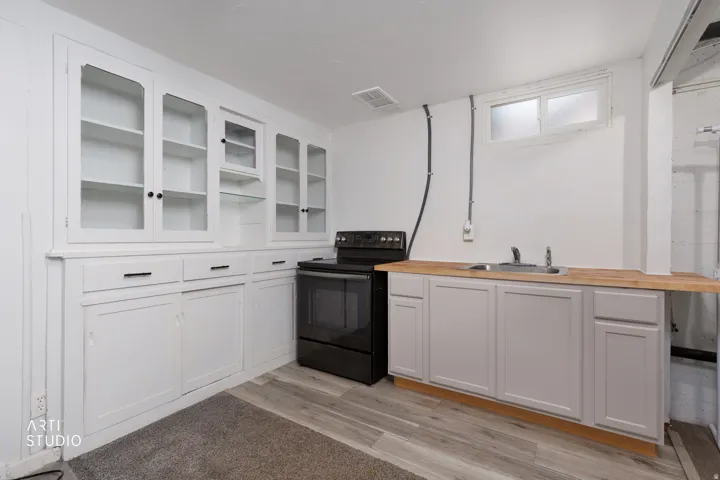 Built-in white cabinetry with glass display doors, matte black range, stainless steel sink, wood-finish countertop, and wood-finish flooring