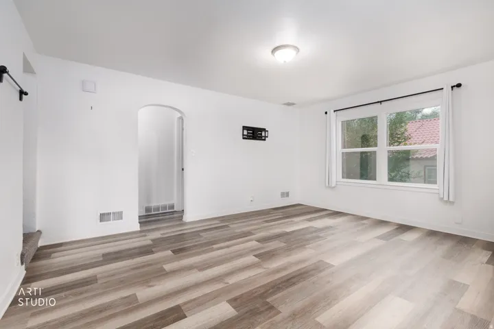 Wood-finish flooring throughout, white painted walls, window with black curtain rod, recessed lighting, and an arched doorway