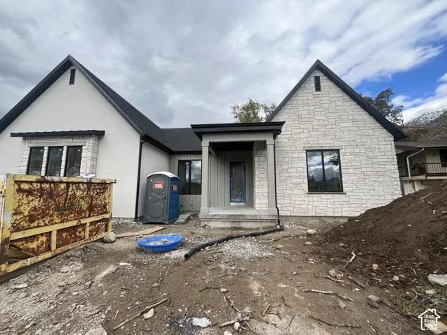 Exterior facade featuring a combination of stone masonry and smooth-finish siding, steep gabled rooflines, dark-framed windows, and a covered front entryway