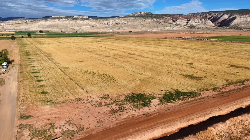 Expansive agricultural land featuring cultivated fields, a dirt road, and distant mountain ranges under a clear sky