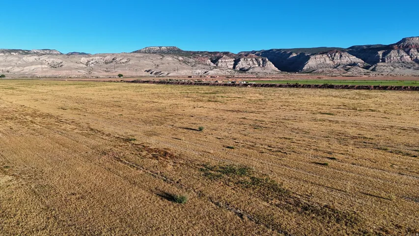 Expansive rural landscape featuring a large field, distant mountain range, and clear sky