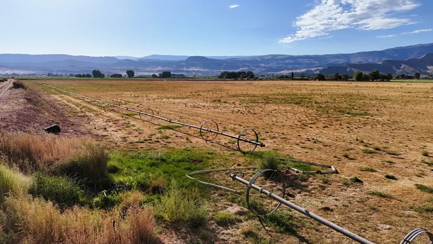 Expansive agricultural land featuring a wheel line irrigation system, a distinct property boundary, and distant mountain backdrops
