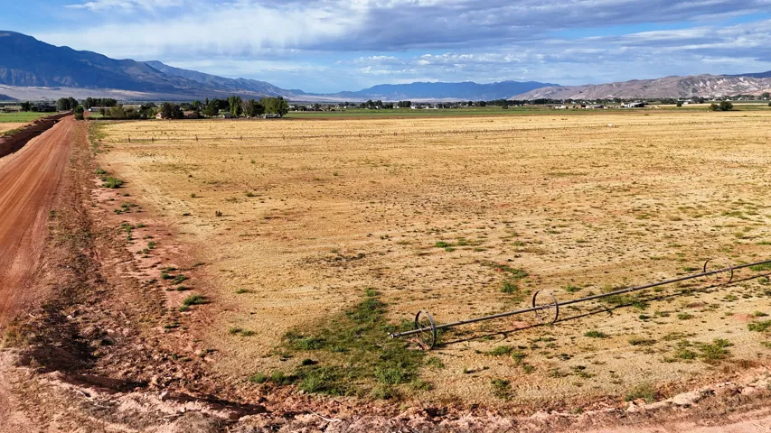Expansive open land with a dirt road, irrigation equipment, and distant mountain scenery