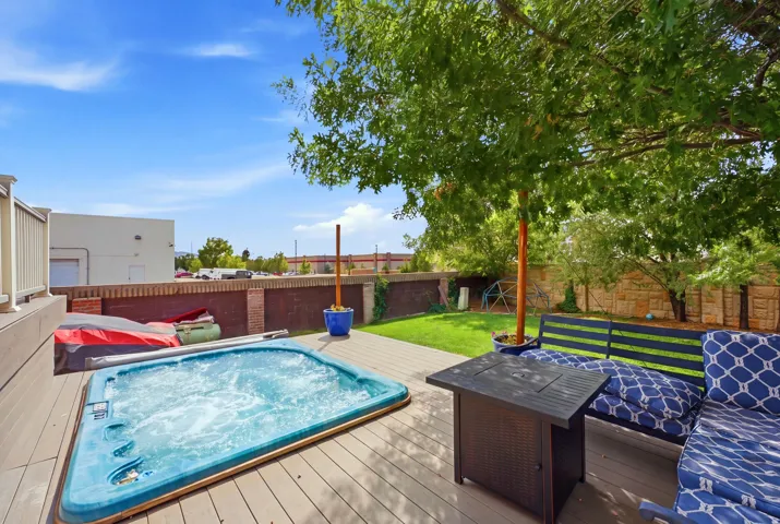 Expansive outdoor deck featuring an in-ground spa, mature shade tree, and a grassy yard area