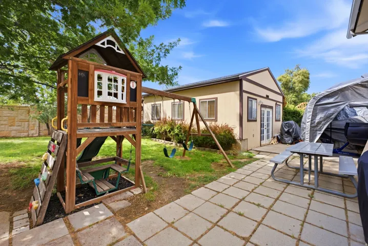 Spacious backyard featuring a stone paver patio, a detached auxiliary building with French doors, and mature trees