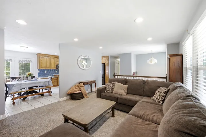 Recessed lighting throughout, carpeted living area, tile flooring in dining space, wood cabinetry in kitchen, and double glass-paneled doors