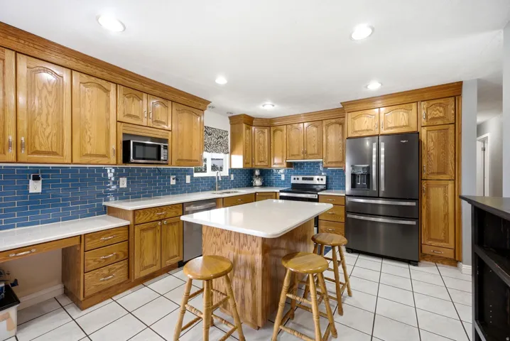 Kitchen featuring extensive wood cabinetry, white tile flooring, a central island with countertop, a blue subway tile backsplash, and recessed lighting