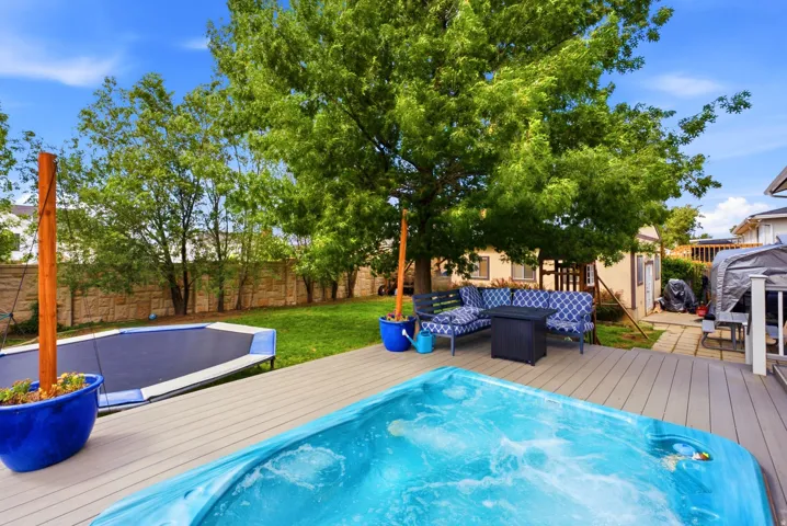 Expansive backyard featuring a hot tub, composite decking, manicured lawn, stone privacy fence, and mature trees