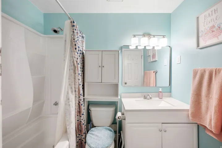 Bathtub with integrated shower, white vanity with integrated sink, wall-mounted mirror, and overhead vanity lighting