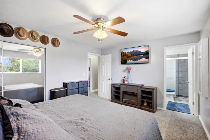Carpeted room with a ceiling fan, mirrored closet doors, and an en-suite bathroom featuring tiled walls