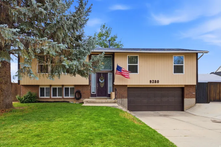 Two-story exterior with a mature front tree, attached garage, and a concrete driveway