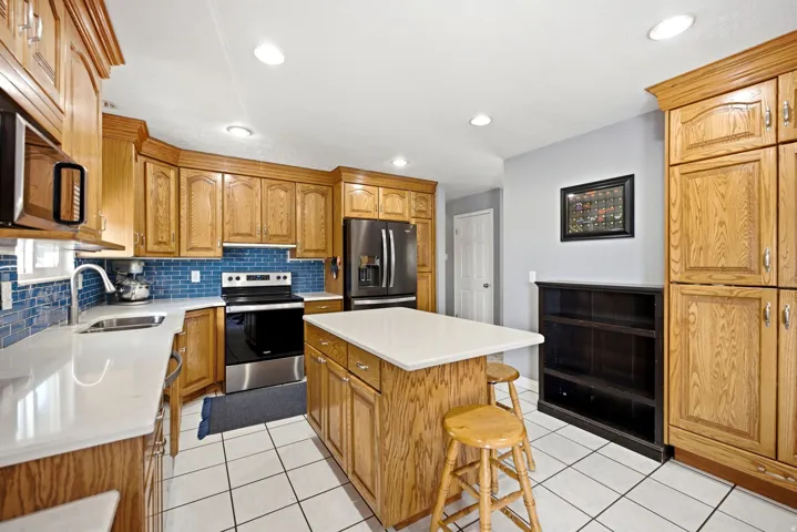 Wood-finish cabinetry with crown molding, stainless steel appliances, white countertops, blue subway tile backsplash, and recessed lighting