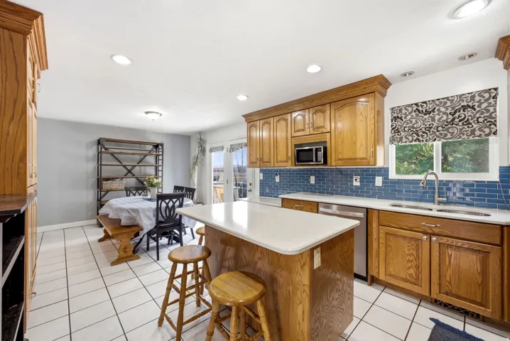 Kitchen featuring wood cabinetry, white tile flooring, blue subway tile backsplash, recessed lighting, and a kitchen island with seating