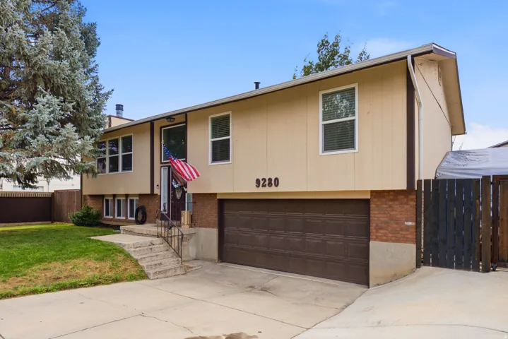 Split-level residence featuring a two-car garage, brick accents, and a mature tree