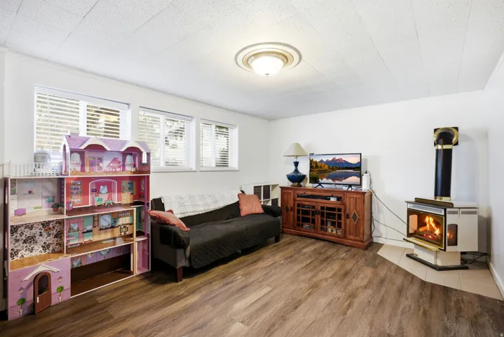 Wood-finish flooring, multiple windows with blinds, ceiling-mounted light fixture, and a built-in corner fireplace with tile hearth