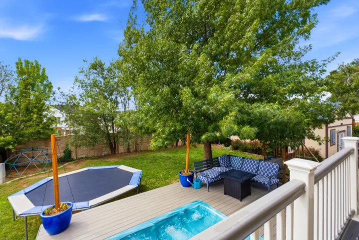 Expansive backyard featuring a hot tub, a spacious composite deck, mature trees, and a privacy fence