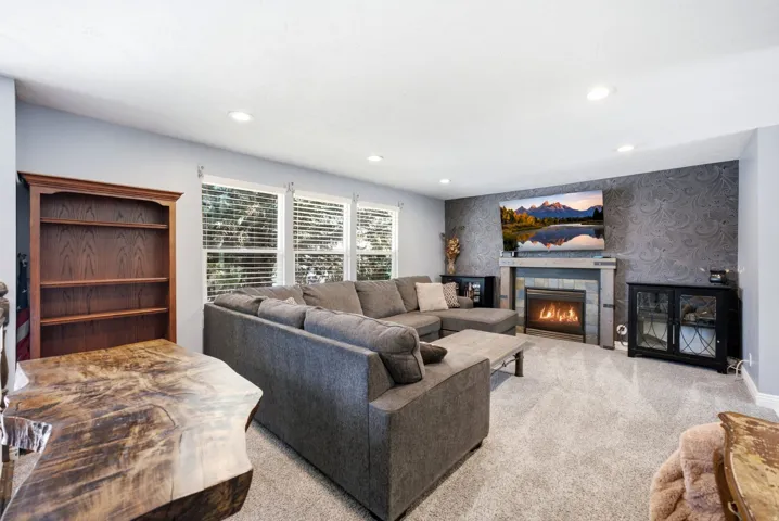 Recessed lighting illuminates carpeted flooring, a built-in gas fireplace with a stone surround, and a textured accent wall