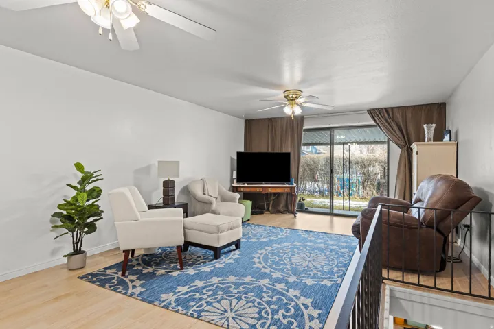 Living area featuring wood-finish flooring, white walls, and a ceiling fan with integrated lighting