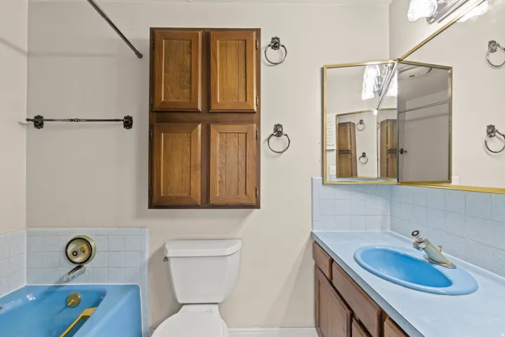 Bathroom featuring a blue bathtub, blue tiled wainscoting, wood-finish cabinetry, a white toilet, and a medicine cabinet with mirror