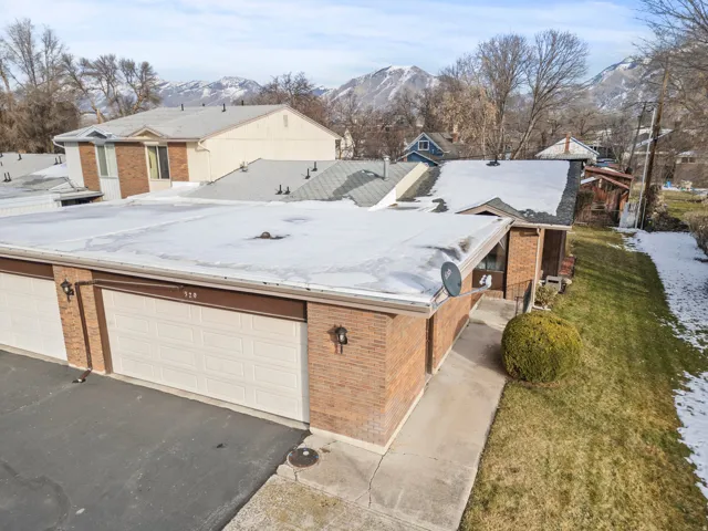 Brick residence featuring a flat roof with white membrane coating, attached garage with white sectional door, and mature landscaping with established trees